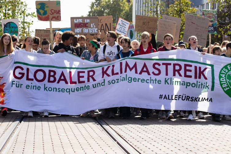 Young people hold a large white banner announcing a 'global climate strike' in German.